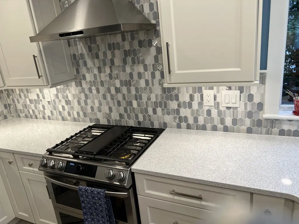 Gray hexagon mosaic backsplash with gas range and white shaker cabinets