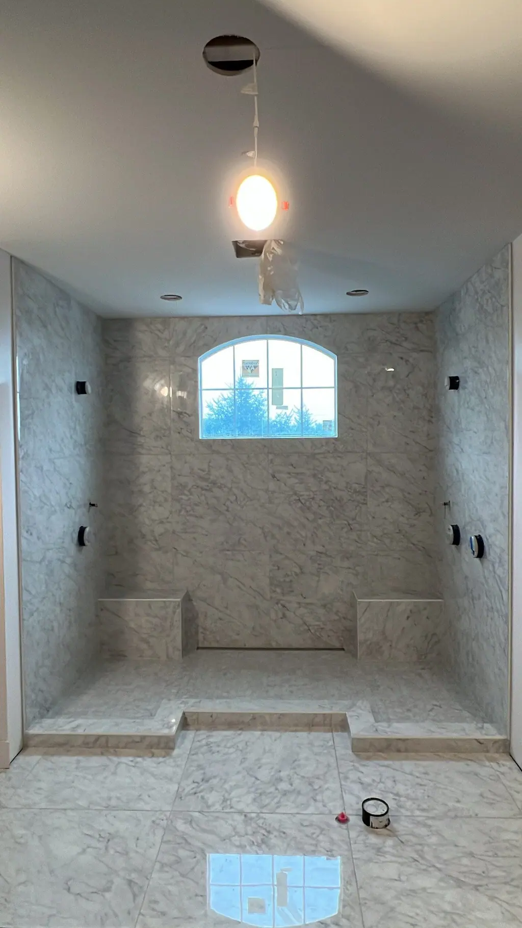 Large marble-look walk-in shower with arched window and built-in bench